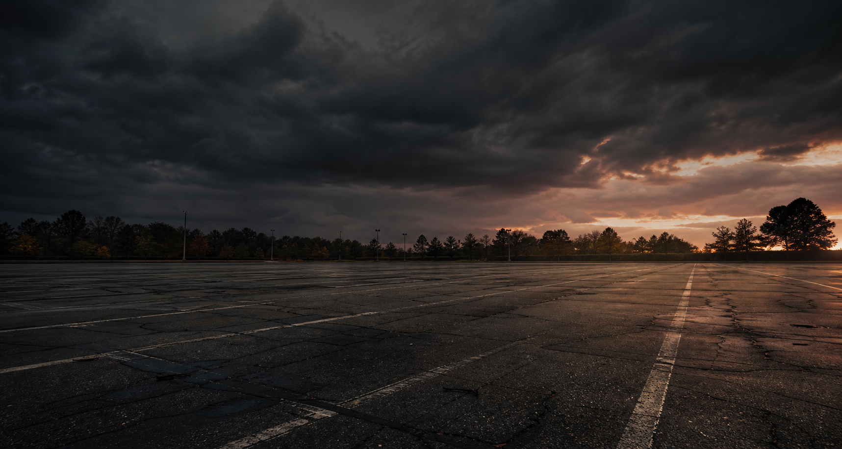 Empty cracked parking lot under a dramatic dark sky.